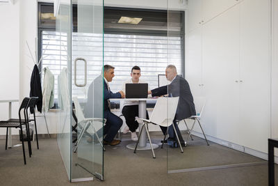 Mature businessman discussing over laptop with colleagues sitting at desk in office