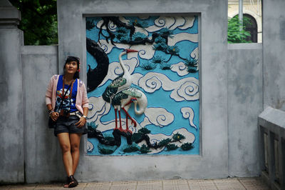 Full length of young woman standing against wall