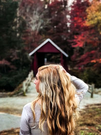 Rear view of young woman with hand in hair standing at park during autumn