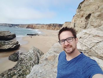 Portrait of man smiling while standing on rocky shore at beach