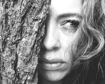 Close-up of young woman looking away by tree trunk