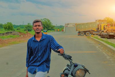 Portrait of young man riding bicycle on road against sky