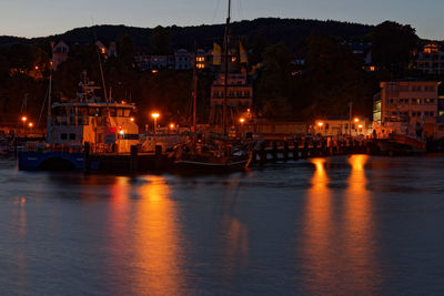 Sailboats moored in sea against illuminated buildings at night