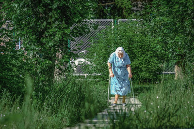 Senior woman walking on steps with canes amidst plants