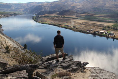 Rear view of man standing on rock looking at river