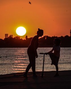 Silhouette men standing on shore against sky during sunset