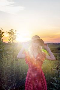 Young woman standing on field against sky during sunset