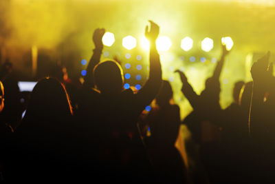 Cheering crowd in front of bright yellow stage lights. silhouette image of people dance in disco 