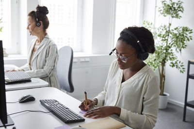 Two women sitting at desk in office and talking via headset