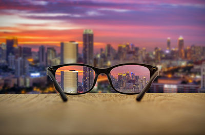 Close-up of eyeglasses on building against sky during sunset