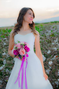 Smiling bride with bouquet standing against sky
