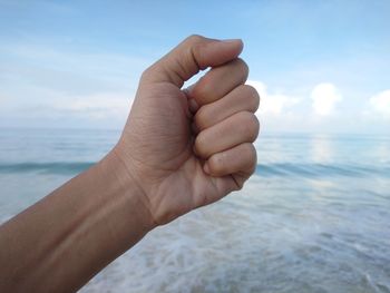 Cropped hand over sea against sky