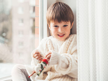 Kid with felt snowman for christmas tree. boy in cable-knit sweater.  red santa claus hat. 