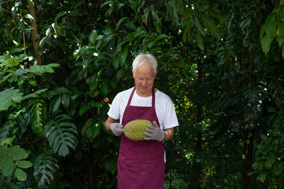 Man holding durian while standing against plants
