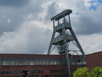 Low angle view of crane by old building against sky