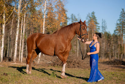 Full length of woman standing by horse at forest