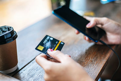 Cropped hands of woman holding credit card and using phone on table