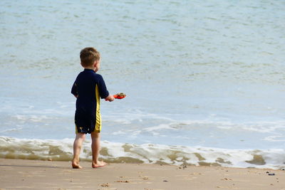 Rear view of boy playing on shore at beach