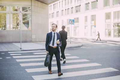Businessman with phone looking away while crossing road in city