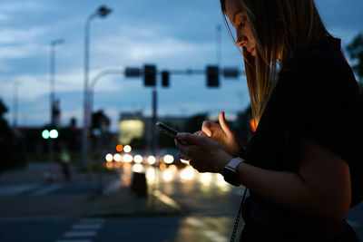 Woman using smartphone on city street with bokeh lights at night. mobile phone in female hands