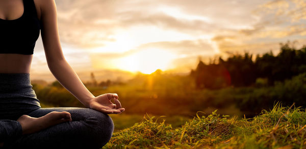 Midsection of man sitting on field against sky during sunset