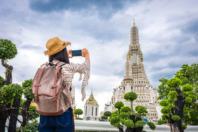 Rear view of man looking at tower against cloudy sky