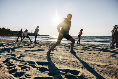Happy woman exercising with team during group training session at beach