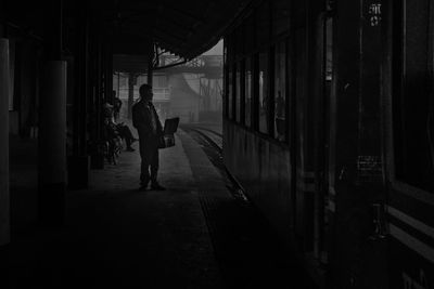 Rear view of silhouette man walking on footpath by building
