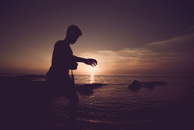 Silhouette man standing on beach against sky during sunset