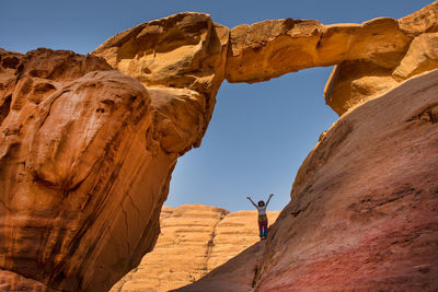 Woman standing on rock formation against clear sky