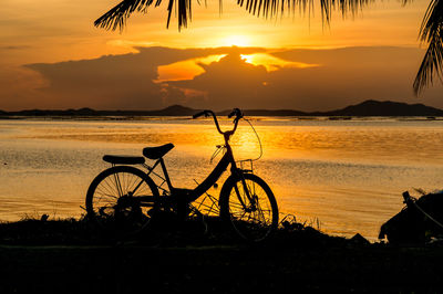 Silhouette bicycles on beach against sky during sunset