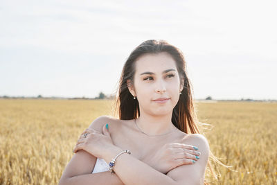 Portrait of young woman sitting on field against sky