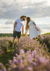 Couple standing amidst purple flowering plants on field against sky
