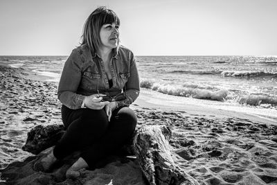 Woman sitting on shore at beach against clear sky