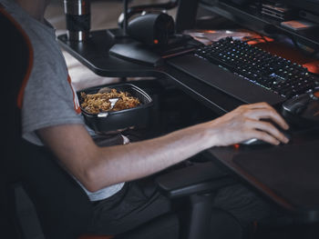 A young caucasian guy gamer holds a black wok food container sitting in a work chair at a table