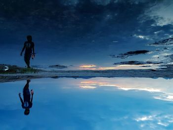 Reflection of man on sea against blue sky