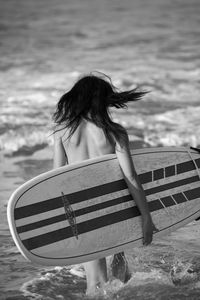 Rear view of young woman holding surfboard while standing in sea