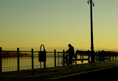 Man on railing against clear sky during sunset