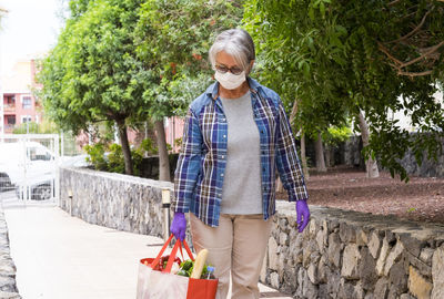 Senior woman holding groceries bag standing by plants