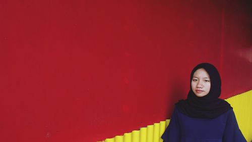 Portrait of smiling young woman against red wall