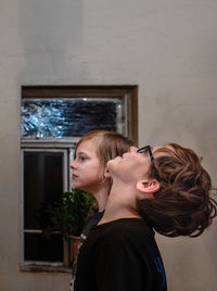 Side view portrait of young woman standing against wall at home