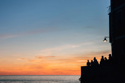 Silhouette people by sea against sky during sunset