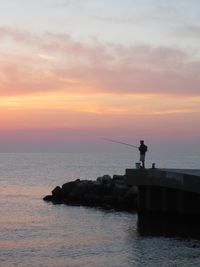 Man fishing from pier during sunset