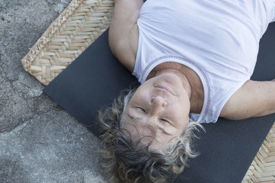 Senior woman lying on yoga mat with closed eyes