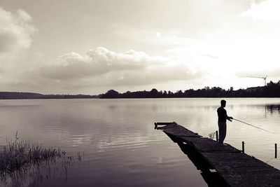 Rear view of man standing on pier over lake