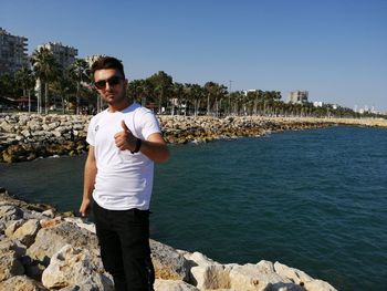 Young man standing on rock against sky