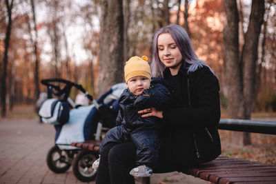 Happy young mother holding baby son while sitting on bench in park