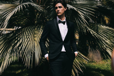 A beautiful young man, the groom in an elegant wedding suit, stands posing in the city's old park