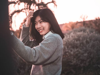 Smiling young woman standing against plants