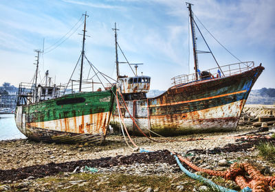 Abandoned boat moored at beach against sky